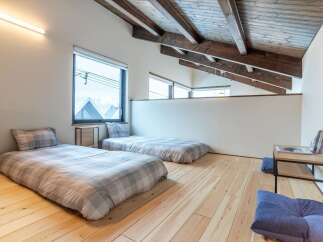 Experience minimalist living in this serene loft bedroom, featuring two comfortable floor beds with plaid bedding.