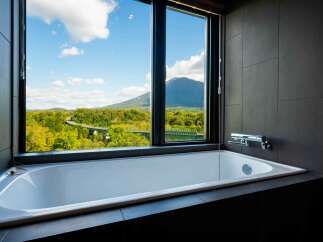 Experience ultimate relaxation in this luxurious bathroom featuring a deep soaking tub with a breathtaking panoramic view of mountains and lush greenery.