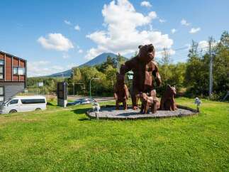 Discover this unique property featuring striking geometric bear sculptures, set against a backdrop of lush green lawns and a majestic mountain.