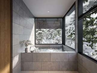 Experience ultimate relaxation in this modern bathroom featuring a luxurious built-in bathtub with stunning views of a serene winter forest.