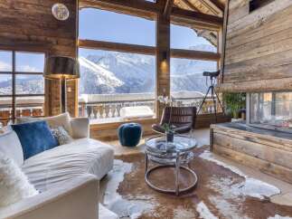 Experience luxury mountain living in this stunning chalet, featuring a cozy living room with a roaring fireplace and expansive windows showcasing breathtaking snow-capped mountain views.