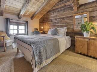 Experience rustic charm in this cozy bedroom featuring exposed wooden beams and a warm, wood-paneled accent wall.
