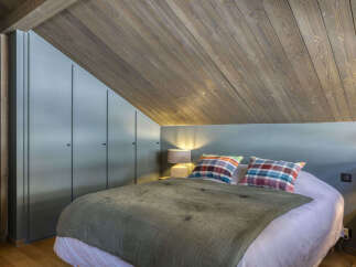 Discover this charming attic bedroom featuring a cozy bed with plaid pillows and a soft green quilt.