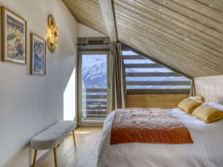 Experience breathtaking mountain views from this charming bedroom, featuring a cozy bed adorned with a warm rust-colored throw and plush yellow pillows.