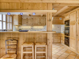 Experience rustic charm in this beautifully appointed wooden kitchen, featuring a breakfast bar with two stools and a comfortable chair.