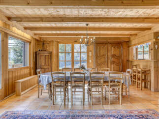 Experience rustic charm in this inviting dining room, featuring a large wooden table draped with a clear protective cover, surrounded by classic wooden chairs.