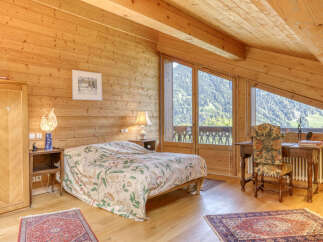 Experience breathtaking mountain views from this charming attic bedroom, featuring a cozy bed with a floral comforter and a rustic wooden wardrobe.