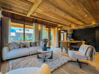 Experience luxurious mountain living in this stunning chalet, featuring a cozy living area with a plush sofa and a rustic wooden ceiling.