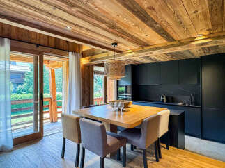 Experience modern alpine living in this stunning property featuring a sleek black kitchen and a warm, wood-paneled dining area.