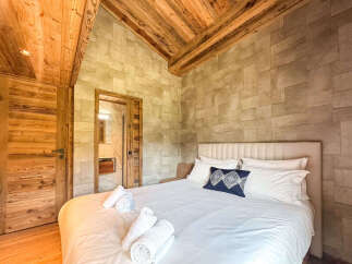 Experience rustic luxury in this charming bedroom featuring a vaulted wooden ceiling and stone-tiled accent wall.