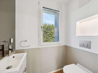 This modern bathroom features a sleek white sink with a chrome faucet, complemented by a wall-mounted towel ring and a discreet toilet paper holder.