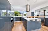 This modern kitchen boasts sleek, high-gloss grey cabinetry and a spacious island with a wooden breakfast bar, perfect for casual dining and entertaining.