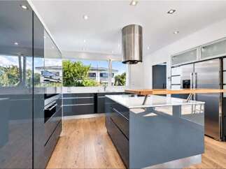 This modern kitchen boasts sleek, high-gloss grey cabinetry and a spacious island with a wooden breakfast bar, perfect for casual dining and entertaining.