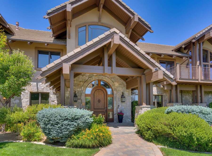 Discover this stunning mountain-style home featuring a grand arched wooden entryway, complemented by exposed timber beams and natural stone accents.
