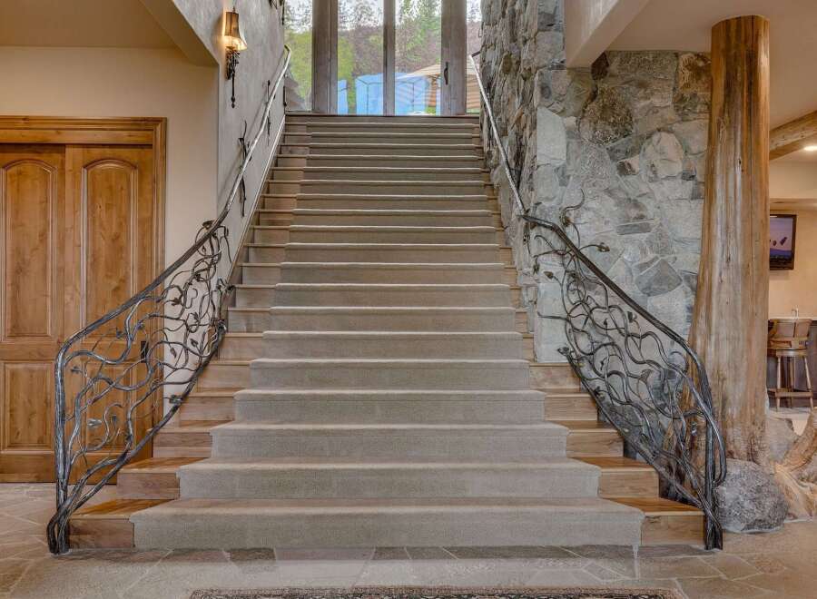 Ascend this grand staircase featuring plush carpeting and intricate wrought-iron railings with a natural, vine-like design.