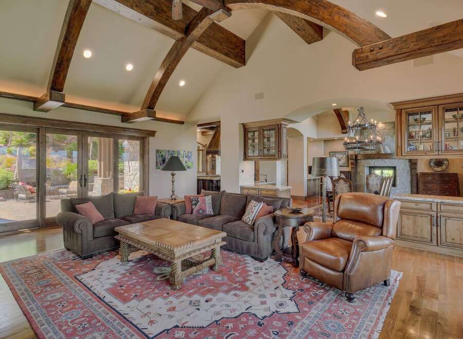 Experience luxury living in this grand living room, featuring soaring vaulted ceilings with exposed wooden beams and abundant natural light from large glass doors.