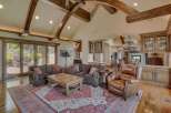 Experience luxury living in this grand living room, featuring soaring vaulted ceilings with exposed wooden beams and abundant natural light from large glass doors.