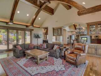 Experience luxury living in this grand living room, featuring soaring vaulted ceilings with exposed wooden beams and abundant natural light from large glass doors.