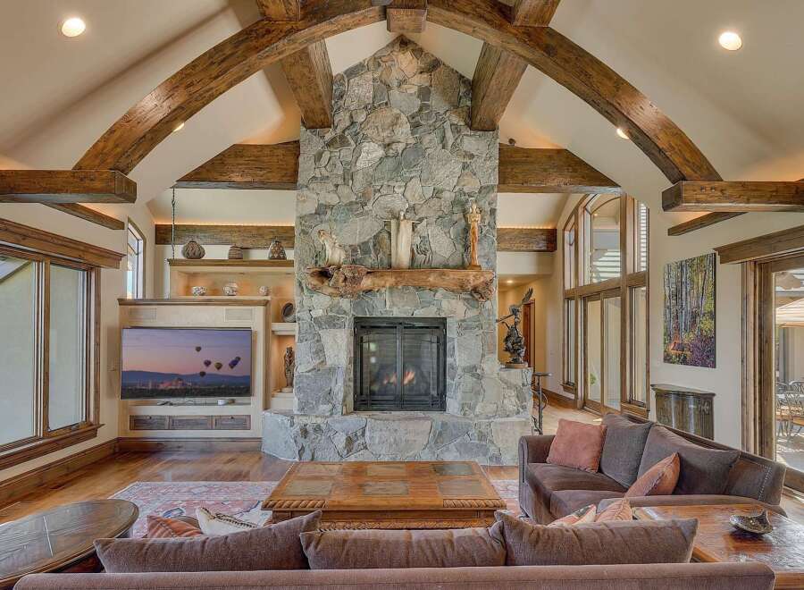 Experience rustic elegance in this stunning living room, featuring a grand stone fireplace with a natural wood mantel and soaring vaulted ceilings with exposed wooden beams.