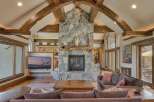 Experience rustic elegance in this stunning living room, featuring a grand stone fireplace with a natural wood mantel and soaring vaulted ceilings with exposed wooden beams.
