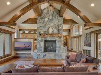 Experience rustic elegance in this stunning living room, featuring a grand stone fireplace with a natural wood mantel and soaring vaulted ceilings with exposed wooden beams.