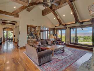 Experience luxurious living in this stunning great room, featuring soaring vaulted ceilings with exposed wooden beams and a grand stone fireplace.