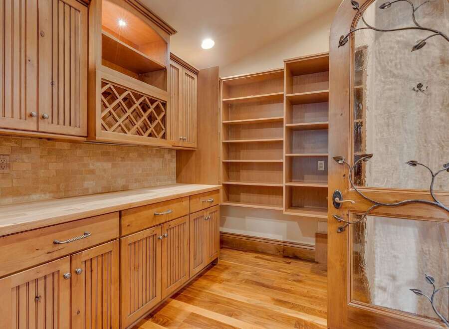 Discover this charming pantry or storage area featuring custom light wood cabinetry, including a built-in wine rack and ample shelving.
