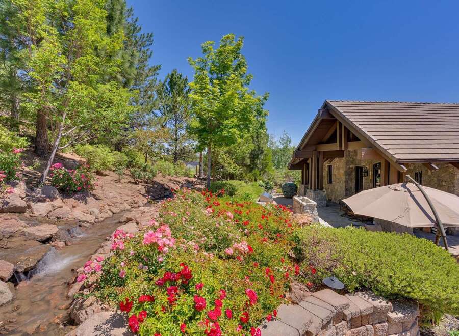 Experience the beauty of this stunning property, featuring a charming stone-accented home nestled amidst lush greenery and vibrant floral gardens.