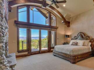 Experience luxury living in this stunning master bedroom, featuring a grand fireplace and expansive windows that offer breathtaking mountain views.