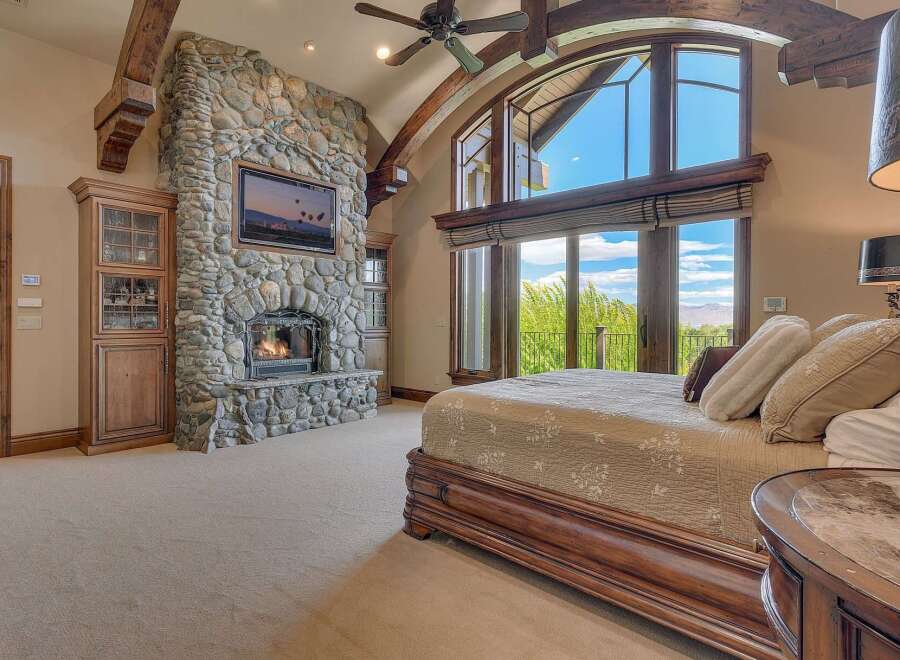 Experience luxury living in this master suite, featuring a grand stone fireplace and a mounted television for ultimate relaxation.