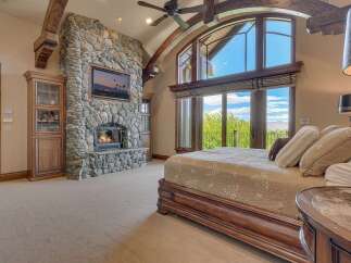 Experience luxury living in this master suite, featuring a grand stone fireplace and a mounted television for ultimate relaxation.