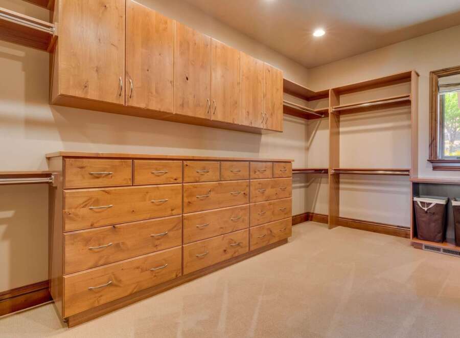 This spacious walk-in closet features ample storage with custom wooden cabinetry, including a long dresser with numerous drawers and overhead cabinets.