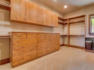 This spacious walk-in closet features ample storage with custom wooden cabinetry, including a long dresser with numerous drawers and overhead cabinets.