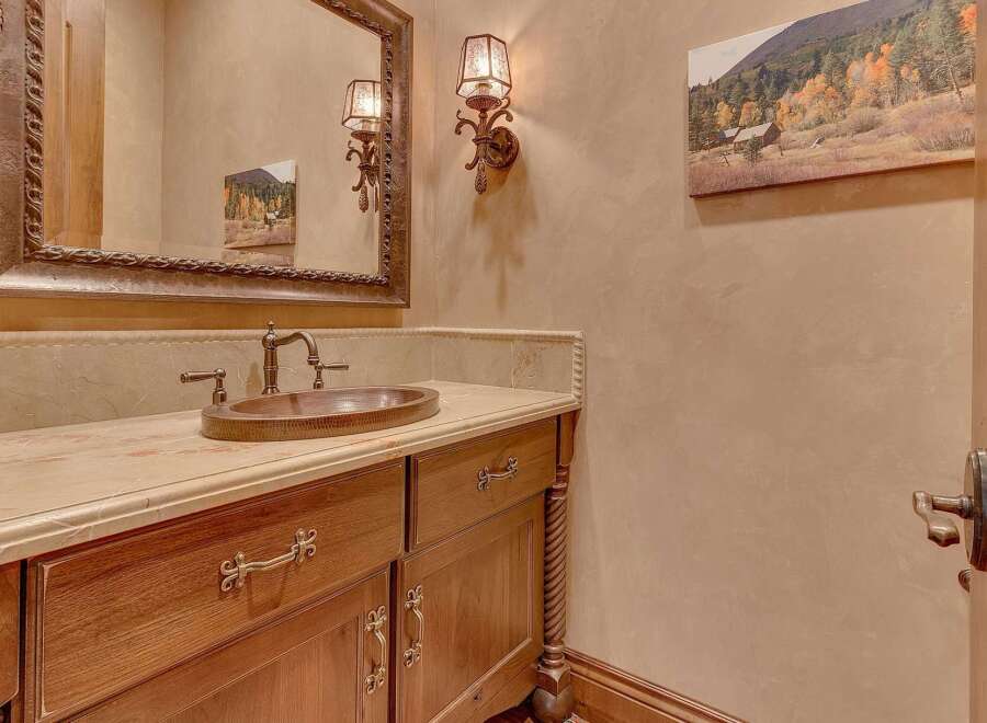 Experience rustic elegance in this powder room, featuring a custom wood vanity with ornate hardware and a hammered copper sink.