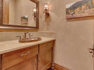 Experience rustic elegance in this powder room, featuring a custom wood vanity with ornate hardware and a hammered copper sink.