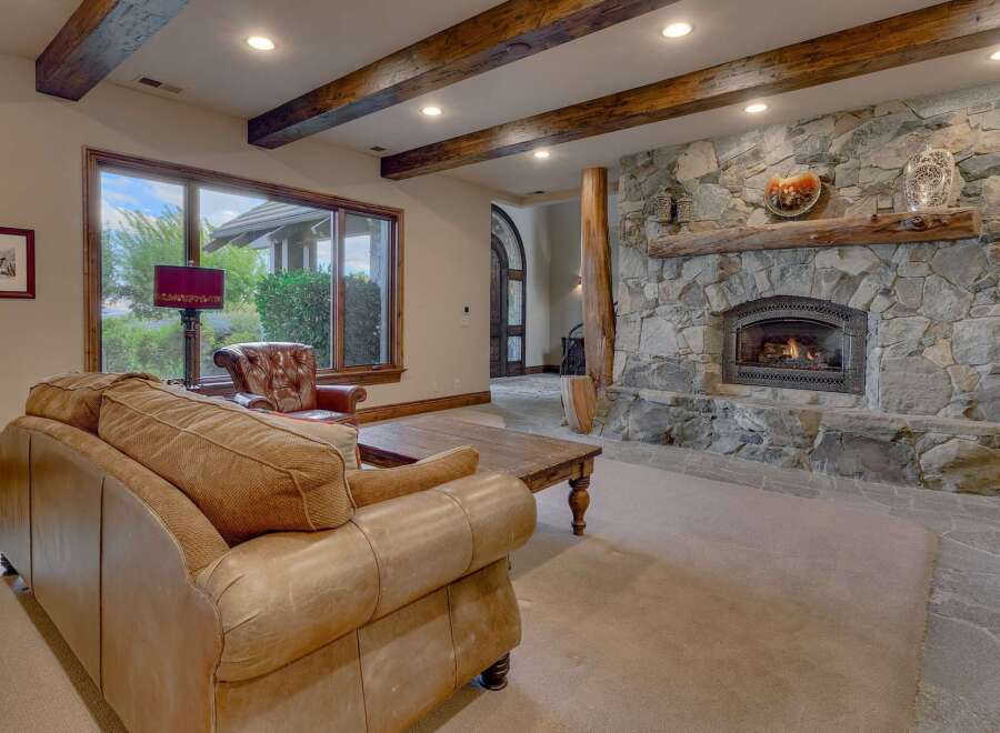 Experience rustic elegance in this living room, featuring a grand stone fireplace with a natural wood mantel and a roaring fire.