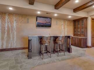 This stunning basement features a custom-built bar area with elegant wooden stools, perfect for entertaining guests.