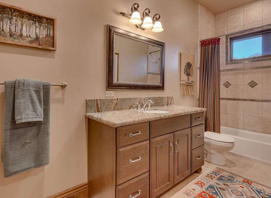 This charming bathroom features a spacious vanity with a granite countertop and ample storage, complemented by a large mirror and elegant lighting.