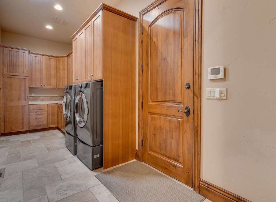 This spacious laundry room features ample storage with custom wooden cabinetry and a convenient side-by-side washer and dryer setup.