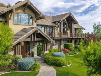 Experience luxury living in this stunning custom-built home, featuring a grand entrance with stone accents and a welcoming wooden door.
