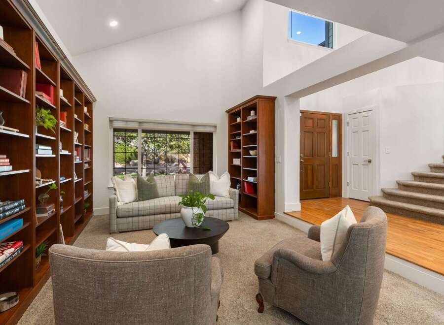 Step into this inviting living room featuring soaring vaulted ceilings and a wall of custom built-in bookshelves, perfect for the avid reader.