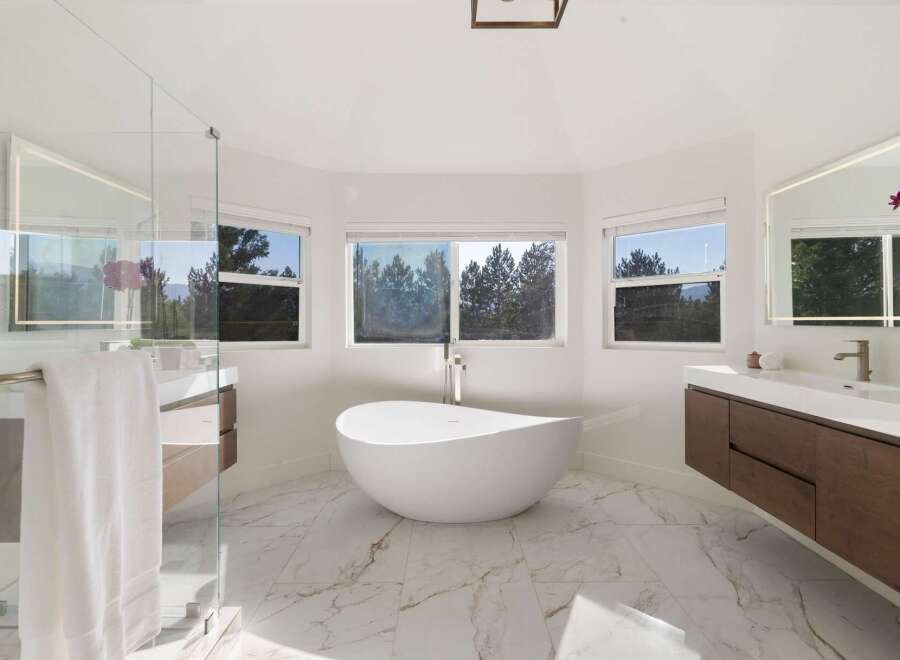 Experience luxury in this stunning modern bathroom featuring a freestanding soaking tub with panoramic views of lush greenery.