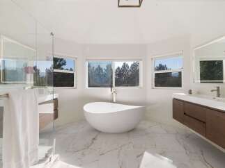 Experience luxury in this stunning modern bathroom featuring a freestanding soaking tub with panoramic views of lush greenery.
