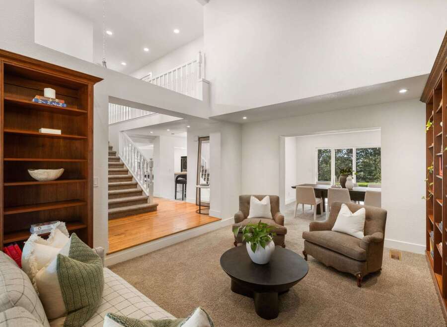This spacious living room boasts a grand two-story layout with a prominent wooden staircase leading to the upper level.