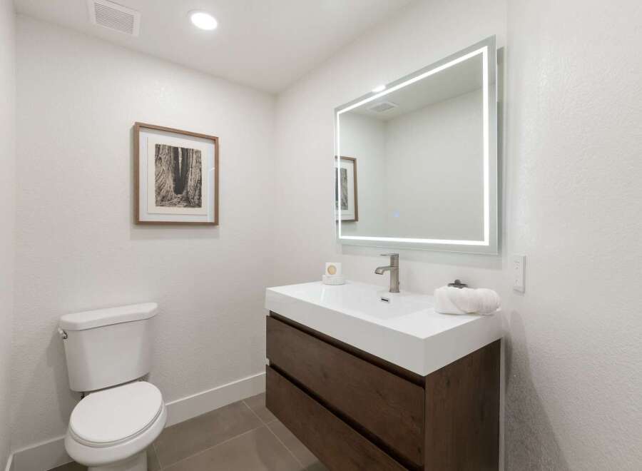 This modern bathroom features a sleek white vanity with dark wood drawers, complemented by a large, illuminated mirror.