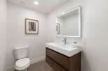 This modern bathroom features a sleek white vanity with dark wood drawers, complemented by a large, illuminated mirror.
