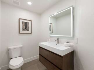 This modern bathroom features a sleek white vanity with dark wood drawers, complemented by a large, illuminated mirror.