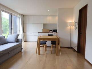 Experience modern living in this bright and airy apartment, featuring a comfortable grey sofa and a sleek dining area perfect for meals or work.