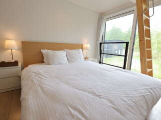 Experience modern comfort in this serene bedroom, featuring a plush king-sized bed with crisp white linens and a minimalist wooden headboard.