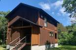 Discover this charming two-story wooden house nestled amidst lush greenery and a clear blue sky.